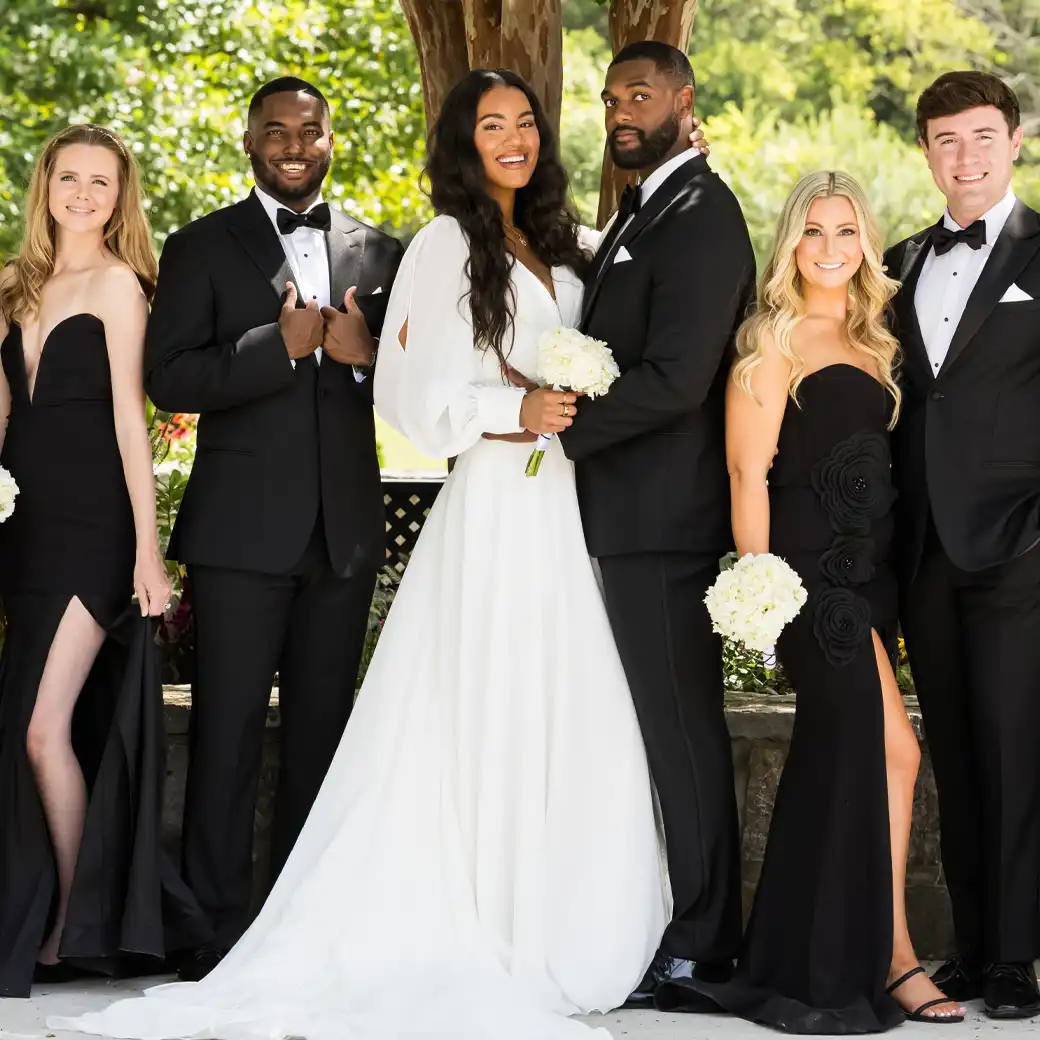 Bride and groom with their wedding party in black tuxedos and black gowns under the trees