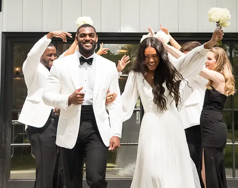 Groom in a white dinner jacket and his bride celebrating with their wedding party