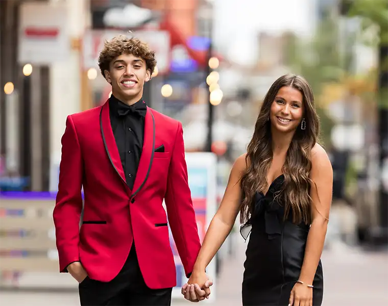 Prom couple, him in a red tuxedo jacket and her in a black dress, walking hand in hand
