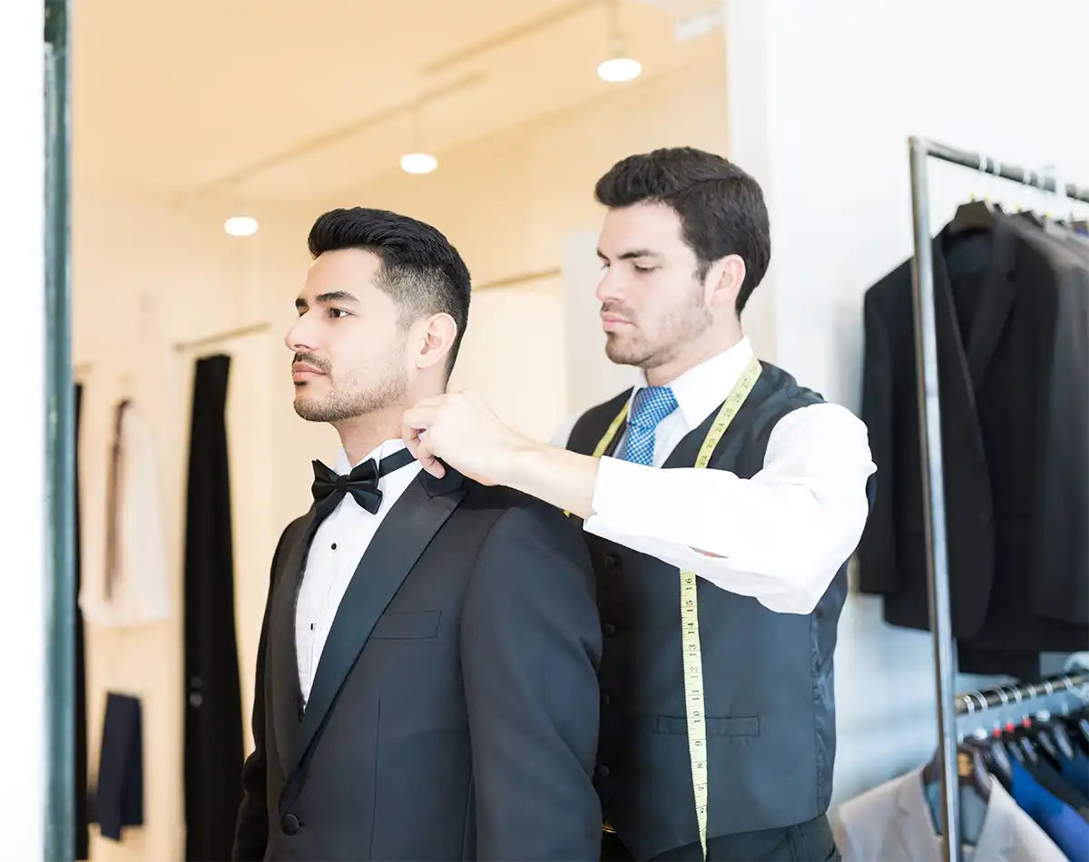 Tailor measuring a groom in a black tuxedo at a formalwear store